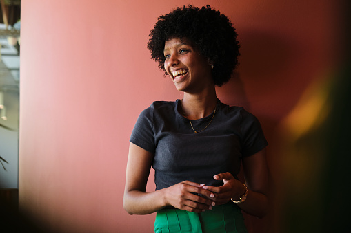 Young businesswoman laughing while leaning with her arms crossed against a red wall in an office