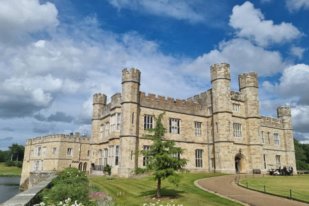 A view of Leeds Castle from an unusual angle with trees and grass in the foreground.