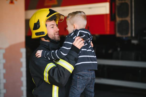 istock A firefighter take a little child boy to save him. Fire engine car on background. Fireman with kid in his arms. Protection concept. 1451387307