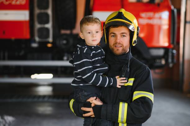 istock A firefighter take a little child boy to save him. Fire engine car on background. Fireman with kid in his arms. Protection concept. 1451387459