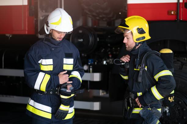istock Two professional firefighters with uniforms and protective helmets posing infront of a firetruck. 1451389821