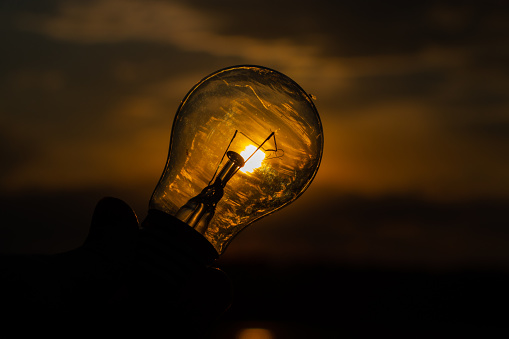incandescent light bulb in hand on sunset background close up