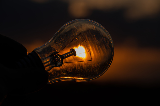 incandescent light bulb in hand on sunset background close -up