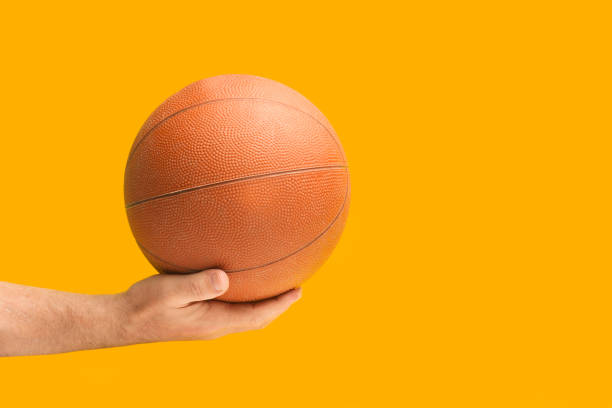 istock Man hand holding a basketball ball on an orange background 1451395010