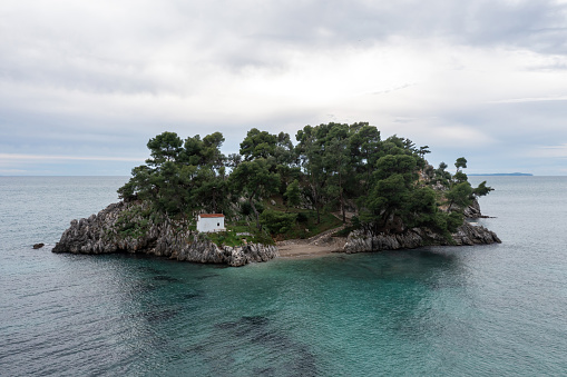 Greece Parga. Panagia island off the coast of Parga, small chapel and trees on the rock, cloudy sky background.
