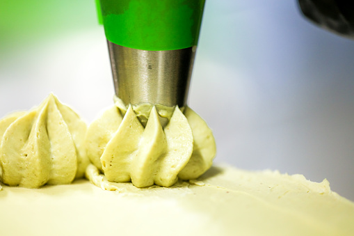 pastry chef designer making swirls with piping bag pistachio cream filling on layered green frosted chocolate cake