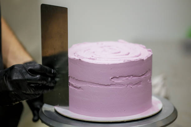istock Decorator using spatula and scraper smoothing and levelling purple lilac buttercream frosted dark chocolate cake 1451399775
