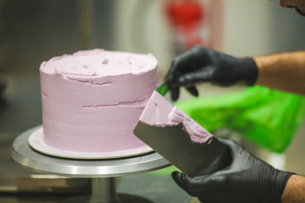 istock Decorator using spatula and scraper smoothing and levelling purple lilac buttercream frosted dark chocolate cake 1451399790