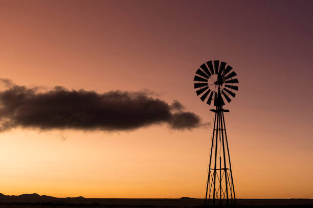 The silhouette of a windmill at sunset with an orange sky and a dark cloud drifting by.