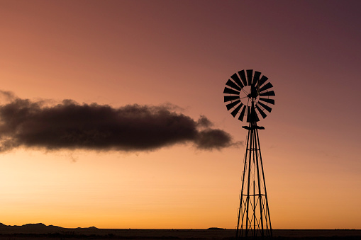 The silhouette of a windmill at sunset with an orange sky and a dark cloud drifting by.