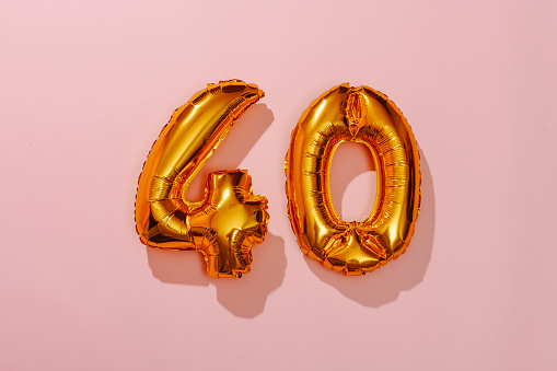 two golden number-shaped balloons forming the number 40 on a pink background
