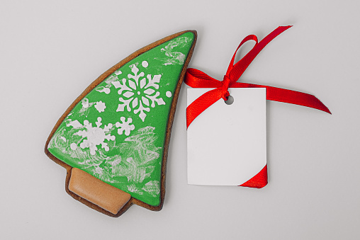 Christmas tree shaped gingerbread cookie and white paper for congratulations text on grey background, top view. Close-up. Happy new year and merry christmas concept
