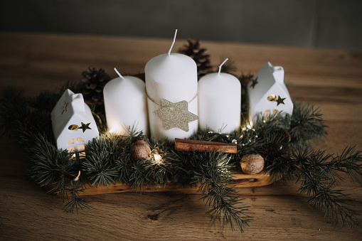 Advent and Christmas decoration, four different lit candles on a rustic wooden tray with fir branches and cookies on a table at the window, copy space, selected focus, narrow depth of field