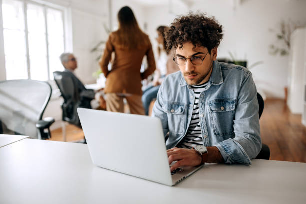 istock Young casually clothed businessman working on a laptop in modern office 1451412383