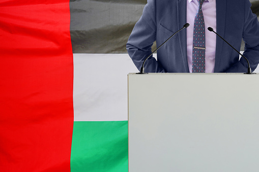 Tribune with microphone and man in suit on flag of United Arab Emirates background. Businessman and tribune on flag of United Arab Emirates background. Business conference in United Arab Emirates