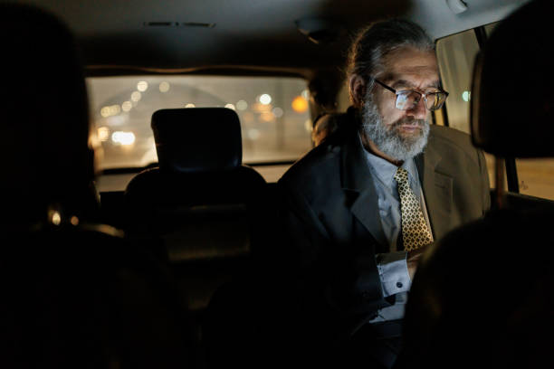 istock Mature businessman using laptop while driving on a back seat in car at night 1451436567