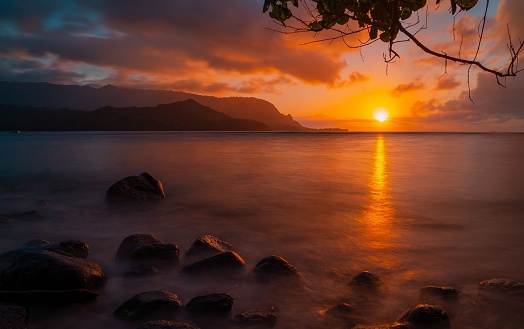 The slanting rays of the sunset at a beach with the silhouette of mountains on the horizon in Kauai,Hawaii