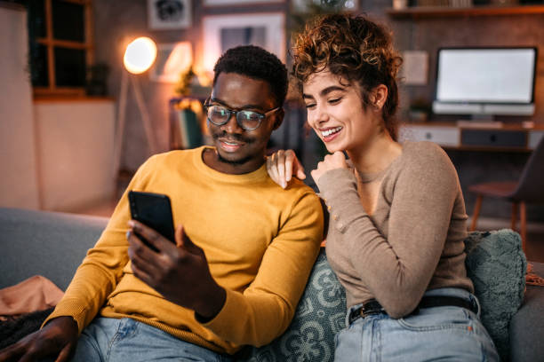 istock Young couple sitting on sofa, surfing the net using smart phone 1451439153