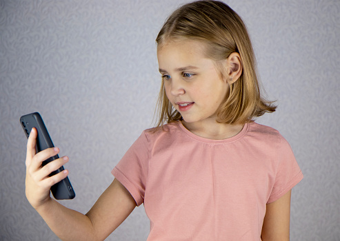 A cute little girl is calling on a smartphone and talking on a video link. Online communication, friendship and vivid emotions of children.