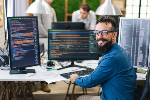 데스크톱 컴퓨터에서 작업하는 웃는 IT 프로그래머. 혁신적인 소프트웨어를 만드는 남성 전문가. 앱, 프로그램, 비디오 게임을 개발하는 엔지니어. 터미널에서 코드 작성 스톡 사진