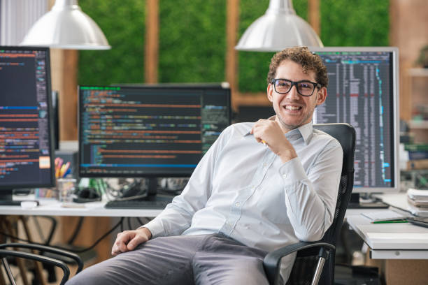 istock Portrait of smiling IT Programmer sitting near Desktop Computers. Male Specialist Creating Innovative Software. Engineer Developing App, Program, Video Game. Writing Code in Terminal 1451457183