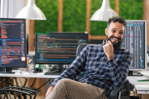 istock Portrait of smiling IT Programmer sitting near Desktop Computers. Male Specialist Creating Innovative Software. Engineer Developing App, Program, Video Game. Writing Code in Terminal 1451457208