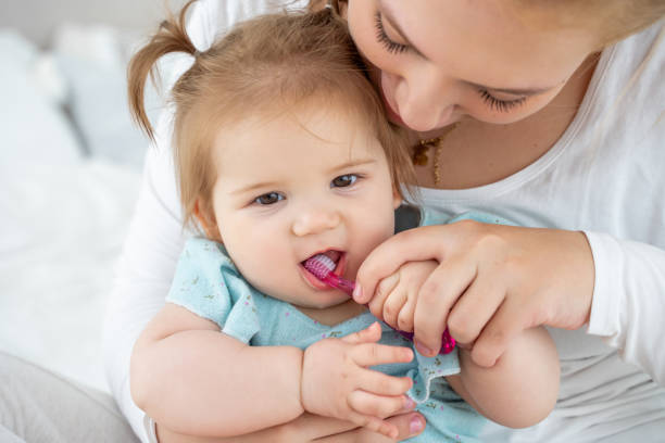 mother brushing baby's first tooth with toothbrush while child laughing. happy education of healthy lifestyle and baby care. babyhood and parenthood. - hairstyle crest imagens e fotografias de stock