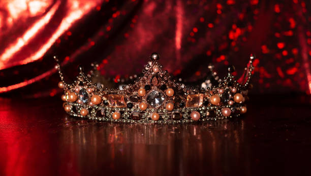 istock Royal crown with precious gems on red luxury fabric background 1451468951