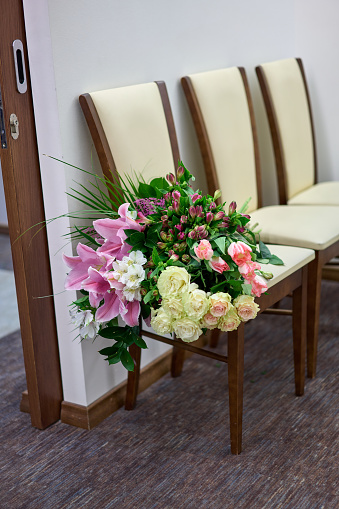 Big colourful flower bouquet on a white chair. Wedding day.