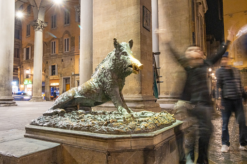 A tourist throwing their hands in the air after rubbing the nose of the wild boar after placing a coin in its mouth to ensure a return to Florence. Il Porcellino (which means 'piglet' in Italian) is the name for this bronze fountain. It was designed by Pietro Tacca (1577-1640) in about 1634. The original; statue represents the Calydonian Boar of Greek myth. It's located at the Mercato Nuovo.