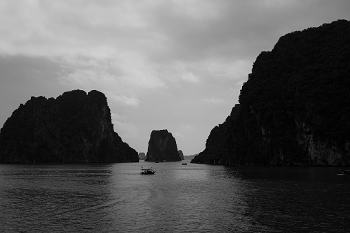A small personal boat makes its way through the impressive karst landscape. Found in Northern Vietnam, the islands that make up the famous Ha Long bay, Vietnam  (black and white)