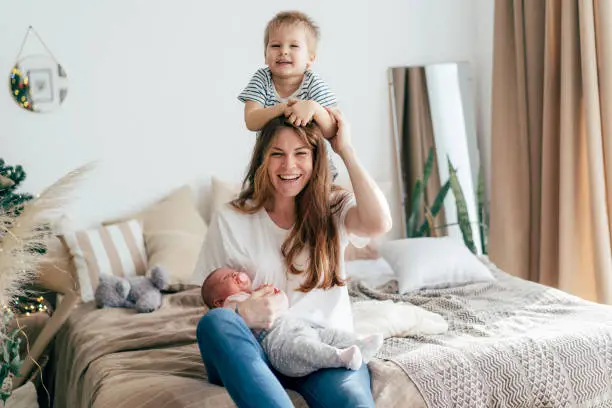 Photo of Cheerful mom with two children laughs and hugs and fools around on the bed in the bedroom.