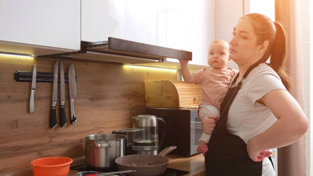 la madre con l'espressione stanca cucina e si prende cura della bambina - mother emotional stress exhaustion cooking foto e immagini stock