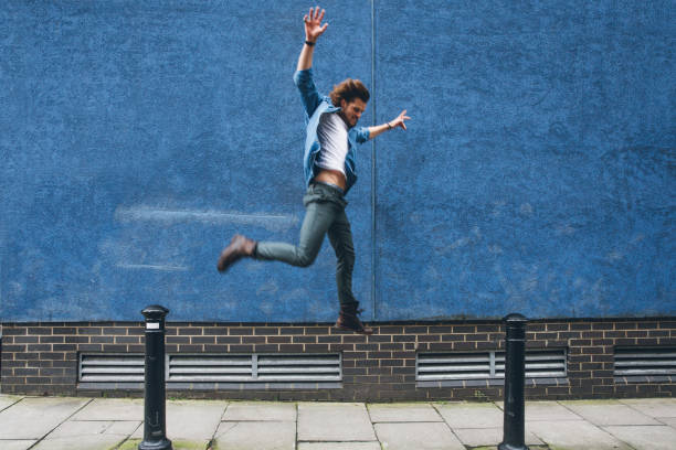 istock Young man in London jumping against a blue wall 1451483155