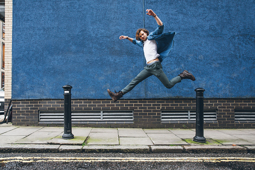 Young man in London jumping against a blue wall.