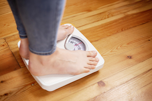 Womens bare feet stand on scales on the wooden floor. The concept of fitness and weight loss tracking