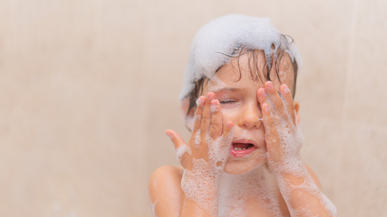 Close-up of little girl playing washing her face with Soap Foam in the bath.