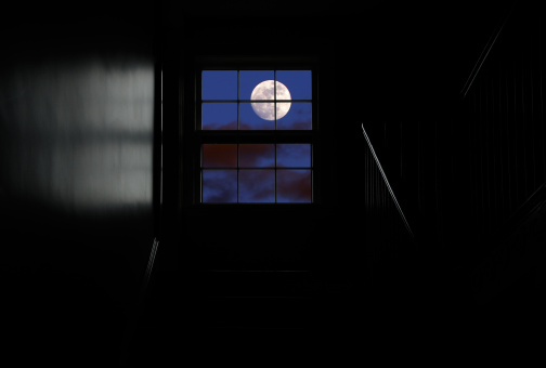 Full moon seen through a window at the top of the stair in a completely dark room