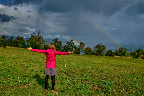 istock Young woman looking at rainbow above valley in rural setting 1451507357