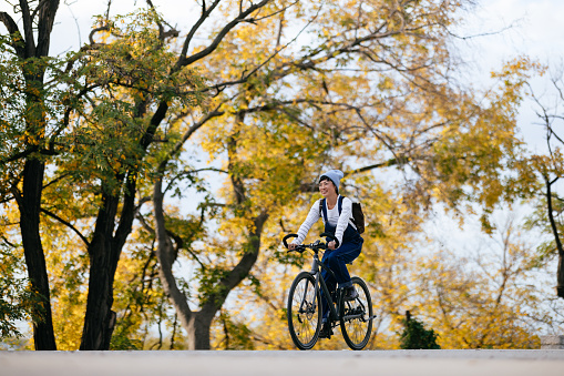 Beautiful smiling Asian woman wearing casual clothes, enjoying riding her bike in the park on a chilly autumn afternoon.
