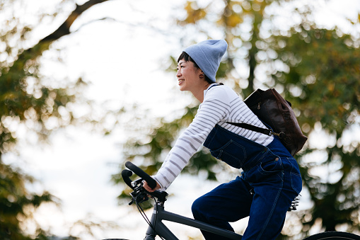 Close up shot of a beautiful smiling Asian woman wearing casual clothes, enjoying riding her bike in the park on a chilly autumn afternoon.