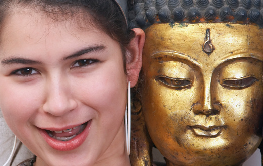 A smiling girl next to a gilded statue of the Buddha.