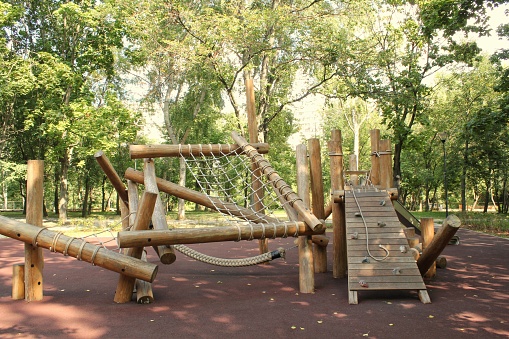 Multicolored Children playground, outdoors play equipment, jungle gym with slide surrounded by a wooden fence, trees in the background. Soft flooring. Galicia, Spain.