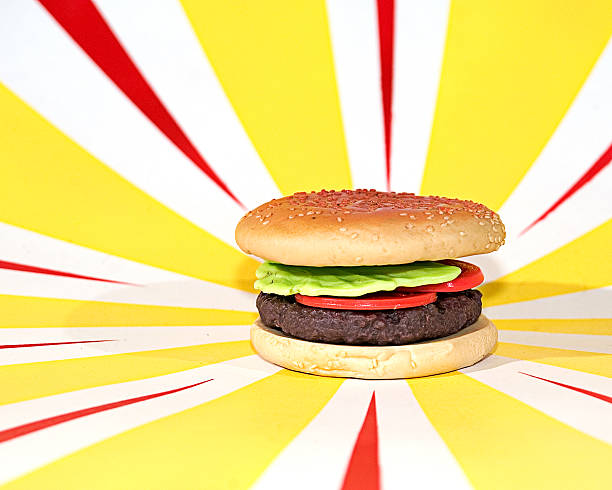 Plastic Hamburger with tomato, lettuce on red and yellow background Plastic hamburger with lettuce and tomato on red and yellow starburst background alagna stock pictures, royalty-free photos & images
