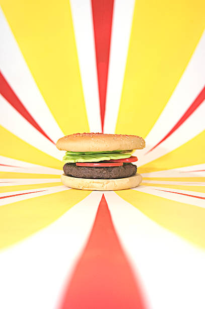 Plastic Hamburger with tomato, lettuce on red and yellow background Plastic hamburger with lettuce and tomato on red and yellow starburst background alagna stock pictures, royalty-free photos & images
