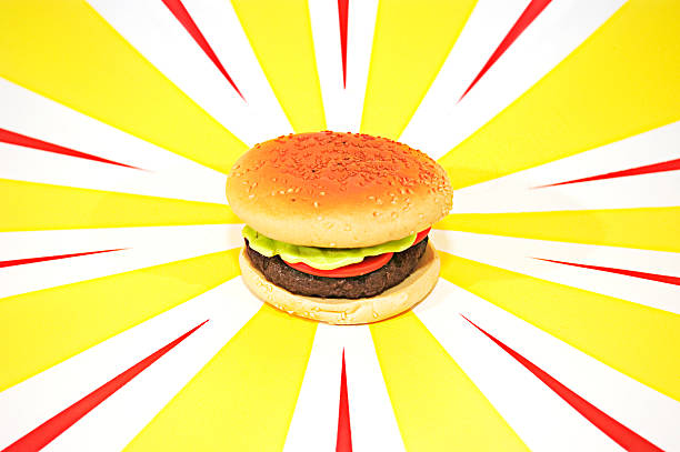 Plastic Hamburger with tomato, lettuce on red and yellow background Plastic hamburger with lettuce and tomato on red and yellow start burst background alagna stock pictures, royalty-free photos & images
