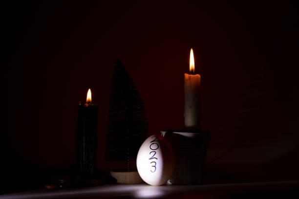 istock 2023 is written on a chicken egg that stands next to a small Christmas tree and candles in the dark without light, a candlelit holiday, there is no light in Ukraine 1451526630