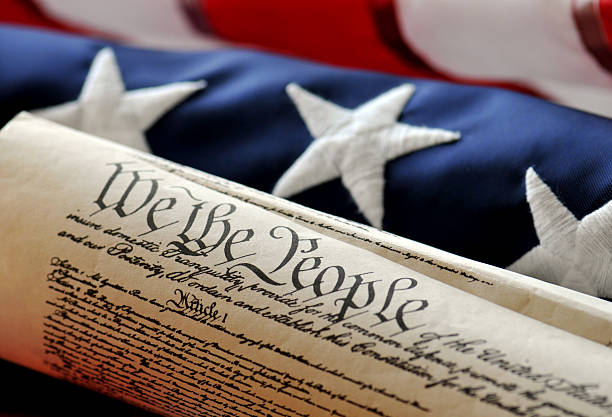 We The People - US Constitution American Constitution with US Flag. Focus on document with stars and stripes in background. philadelphia pennsylvania photos stock pictures, royalty-free photos & images