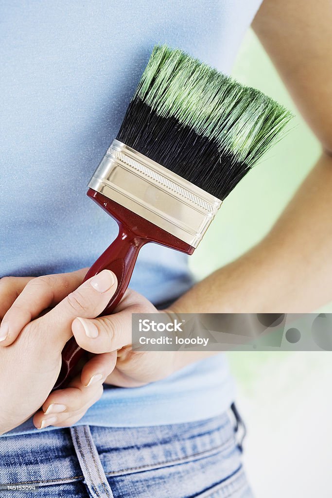painting the house woman holding pait-brush behind her back whilst admiring her work Adult Stock Photo