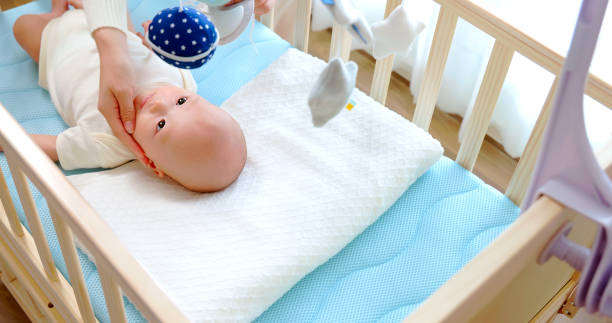 overhead view of asian mother is playing with cute newborn baby who in crib at home and he watching toys which hanging above cot